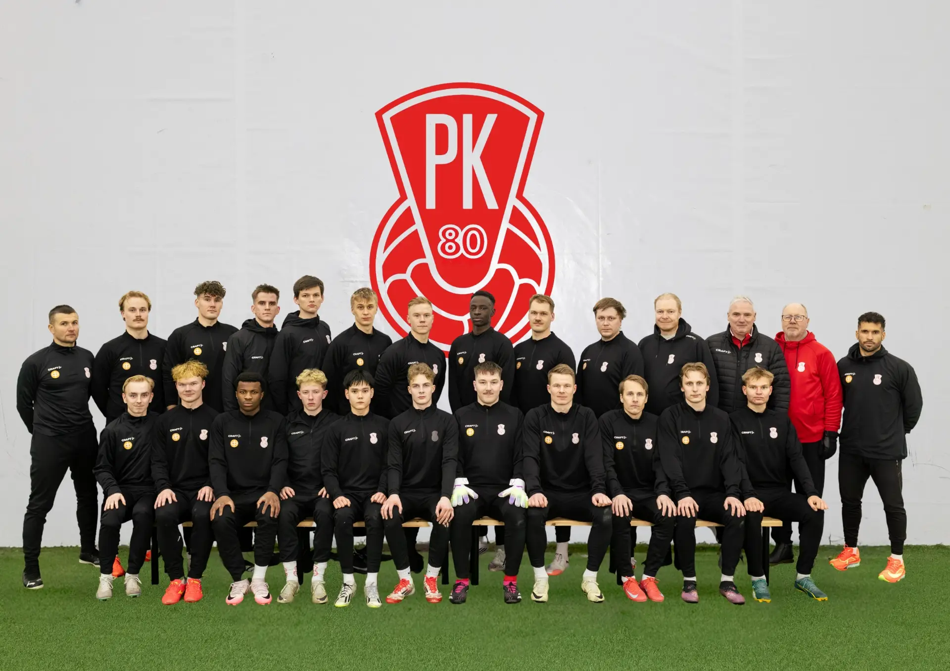 Mikkelin Pallo-Kissojen edustusjoukkueen joukkuekuva. Taustalla on seuran punavalkoinen logo ja pelaaja ovat pukeutuneet mustaan urheiluasuun. Seuran peliasun väri on kotipeleissä punainen ja vieras peleissä musta.